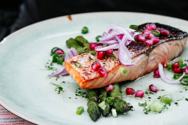 Plate of seared salmon filet with onion, pomegranate seed and asparagus